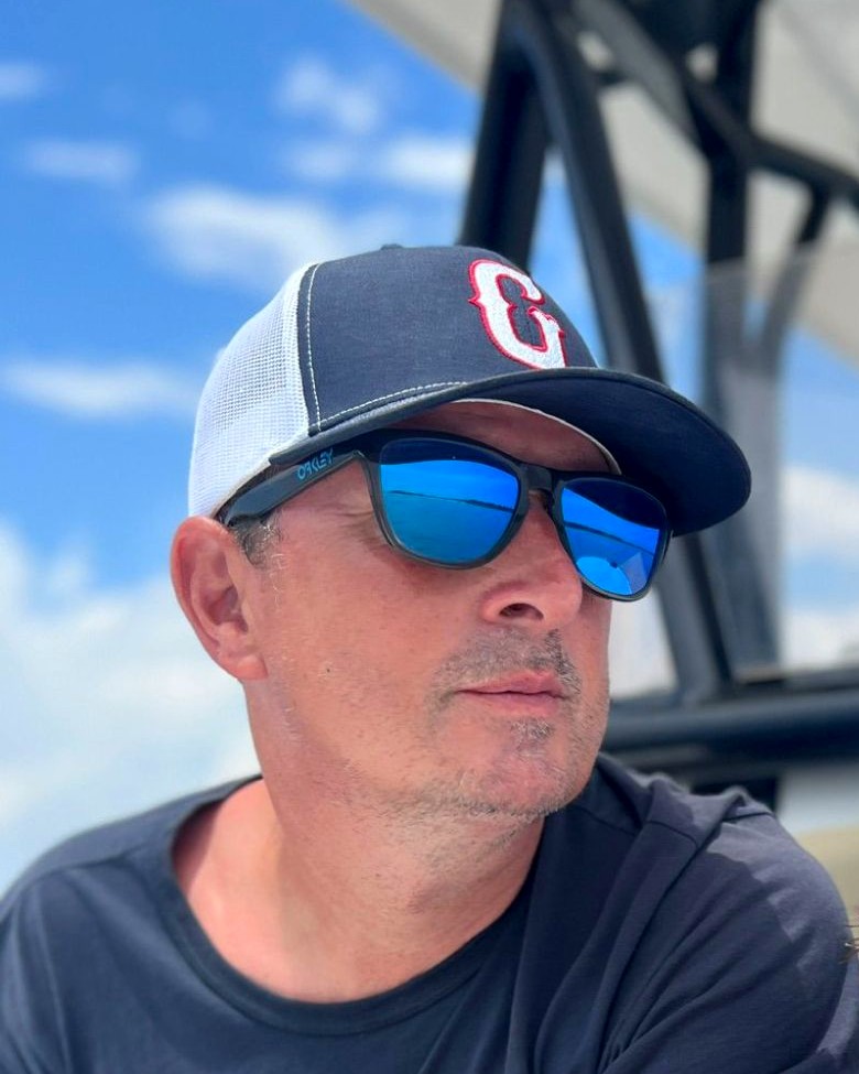 Spencer Wilkinson in a Greenville cap and sunglasses under a summer sky